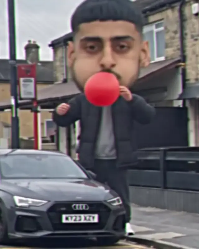A man with a giant head blowing up a red balloon on a Bradford street